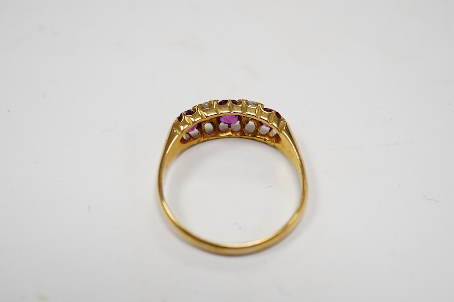 A late Victorian 18ct gold and three stone ruby set half hoop ring, with four stone diamond chip spacers, size P/Q, gross weight 3.2 grams. Condition - poor to fair